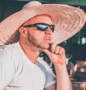 Photo of Carl Neumann wearing a big hat and sunglasses gazing out at the ocean